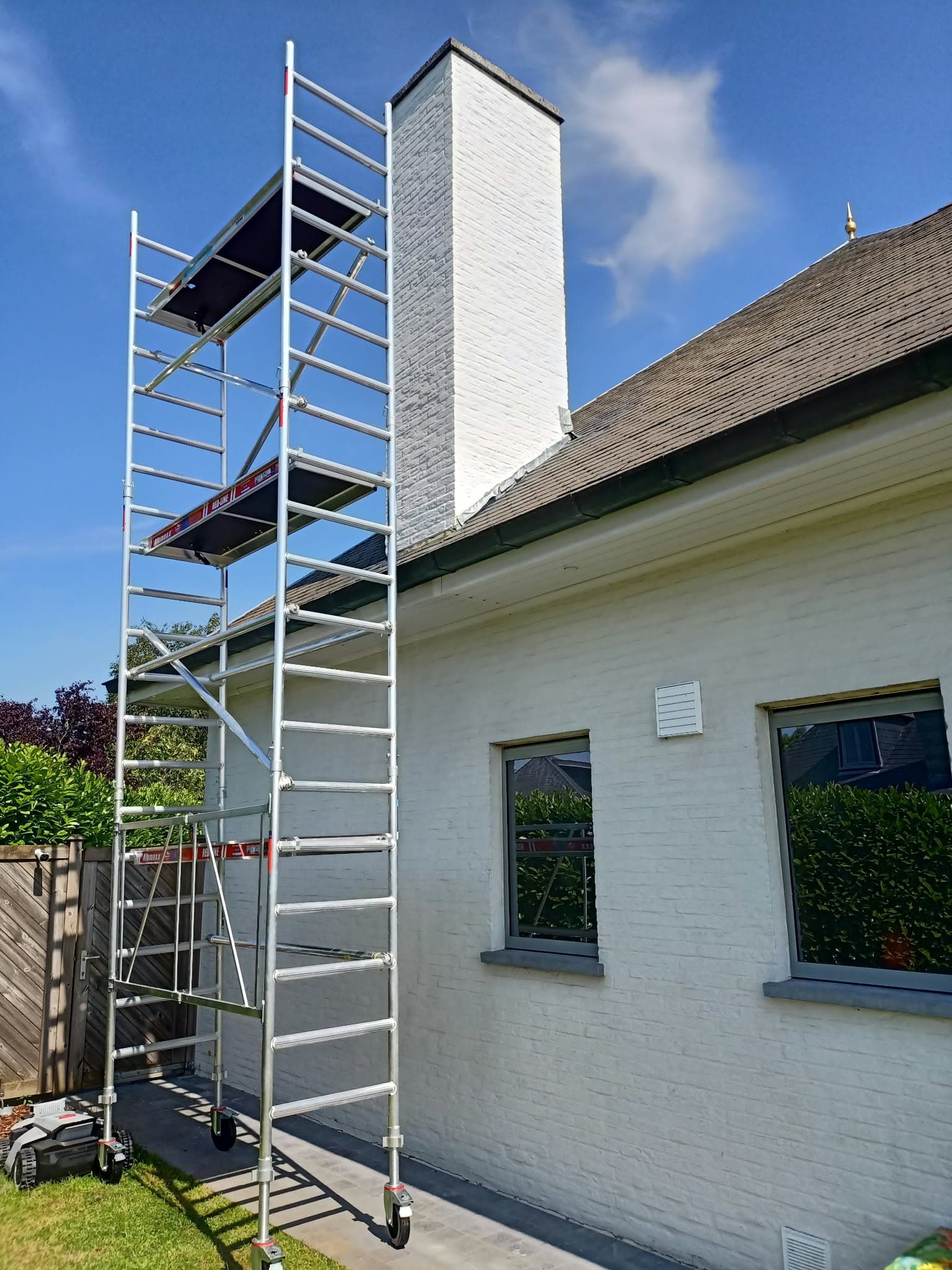 Échafaudage en aluminium à plusieurs niveaux dressé contre une maison blanche avec une grande cheminée.